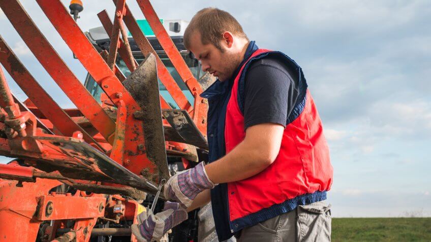 Young mechanic fixing plow on the tractor.