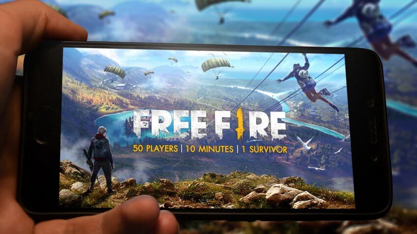 Kyiv, Ukraine; May 11, 2019: Hand holding phone with Free fire logo displayed in it with fluctuating graphic on background.