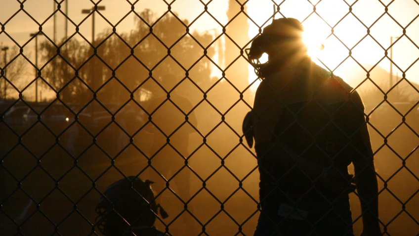 A sunset silhouetted umpire talking to a little league catcher.