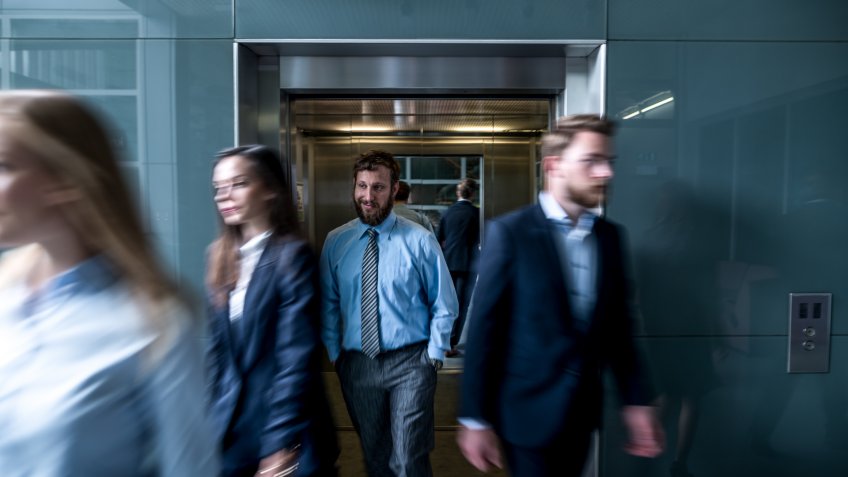 Business people walk out of the lift in the lobby.