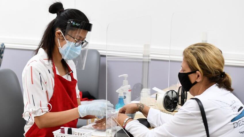 Mandatory Credit: Photo by Larry Marano/Shutterstock (10651183au)A nail salon employee works on a customer through a plexiglass shield at KC Nail Spa as Barber Shops, nail salons and restaurants re-open in accordance with Broward County's Phase 1 during the Coronavirus COVID-19 pandemicCoronavirus outbreak reopening, Coral Springs, Florida, USA - 18 May 2020.