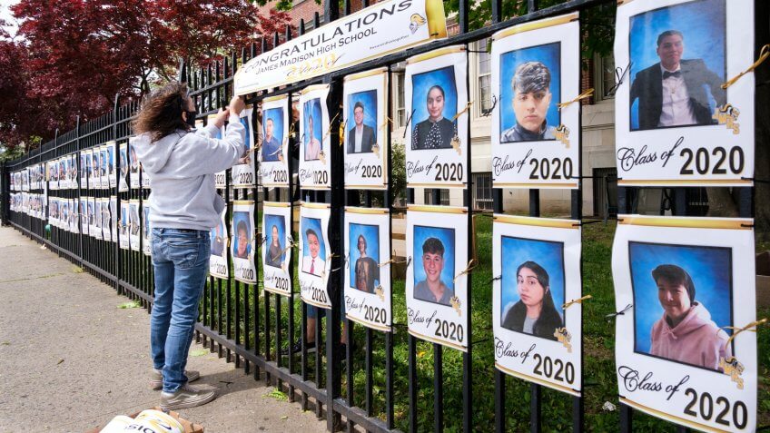 Mandatory Credit: Photo by JUSTIN LANE/EPA-EFE/Shutterstock (10652014d)School employee Luz Carlson hangs a sign over pictures of the graduating senior class displayed on the fence at James Madison High School in Brooklyn, New York, USA, 19 May 2020.