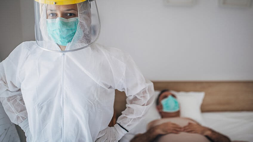 Man and woman, senior man lying in hospital bed because of coronavirus infection, female doctor in standing next to him.
