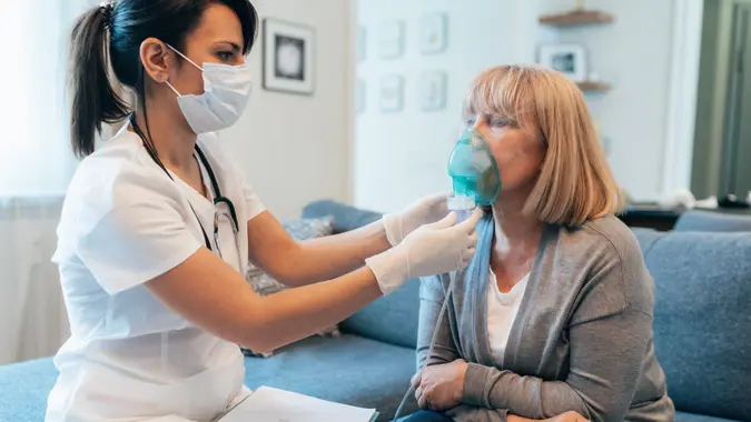 Medical doctor applying medicine inhalation treatment on senior woman by the mask of inhaler during coronavirus quarantine.