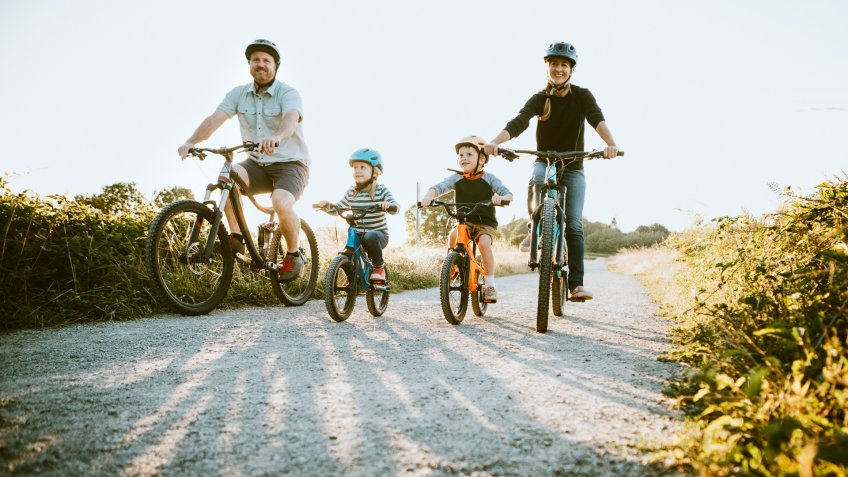 A father and mother ride mountain bikes together with their two small children.