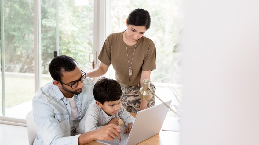 A preschool age boy concentrates as his dad shows him how to do something on a laptop.
