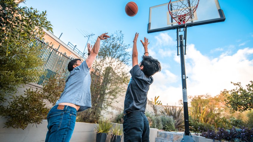 Father and son with arms raised playing basketball.
