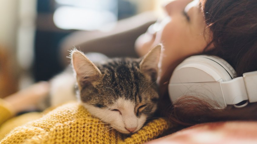 Gen Z girl with eyes closed hugging a cat and enjoying music.