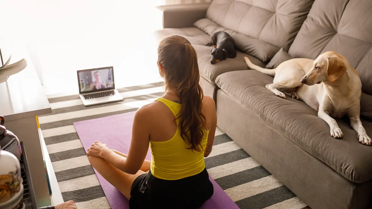 Woman practicing yoga with trainer via video conference.
