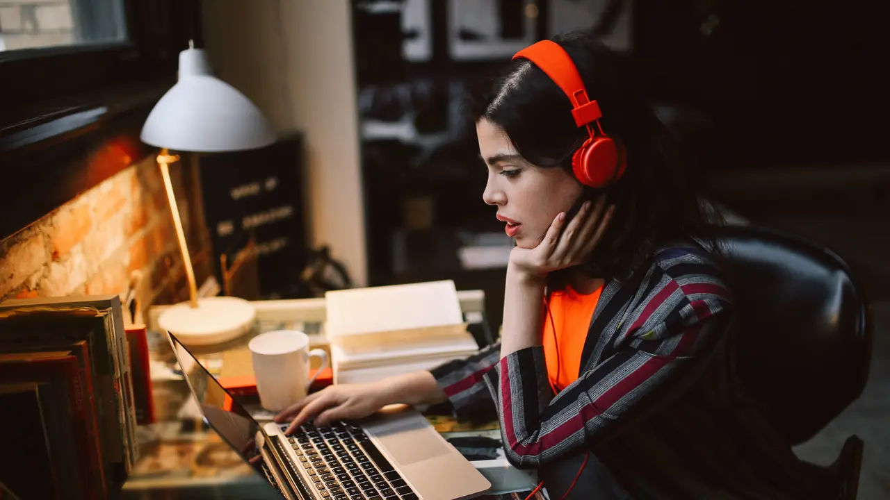 Young Latinx woman sitting at the desk in her Los Angeles apartment, working on the laptop or just having a nice day, listening to the music.