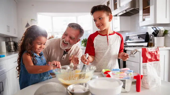 Brother and sister standing at the kitchen table making cake mix with their grandfather.