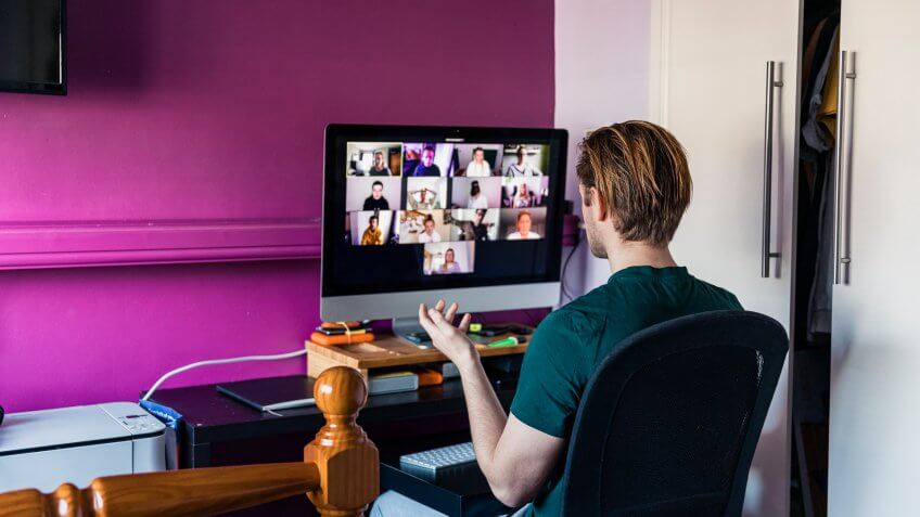 Young caucasian man on a team conference call on a computer screen at his desk in a home office.