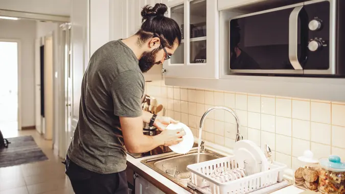 Young man washing dishes at home.