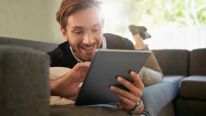 Full length shot of a handsome young man using a digital tablet while relaxing at home.