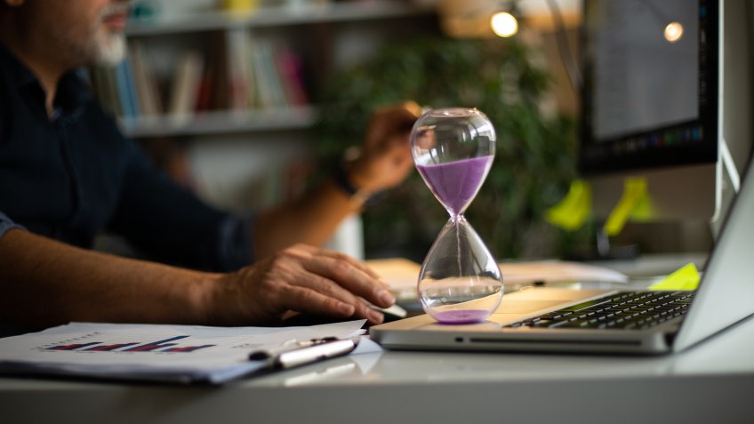 Business concepts with businessman holding hourglass with graph chart on computer laptop.