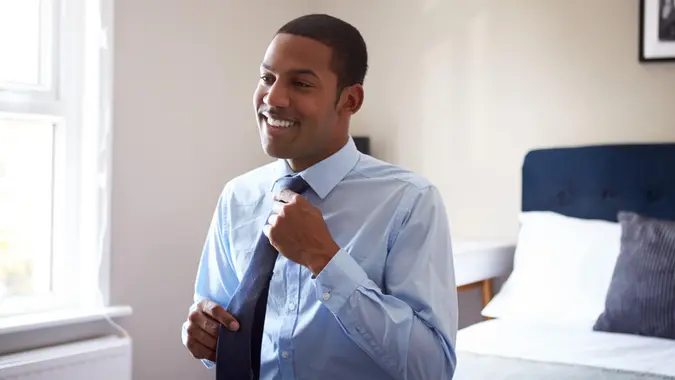 Young Man Getting Dressed In Bedroom For First Day At Work In Office.