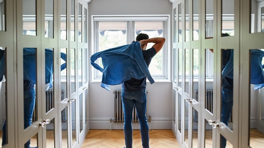 Shot of a man getting dressed in a long walk in closet full of mirrors.