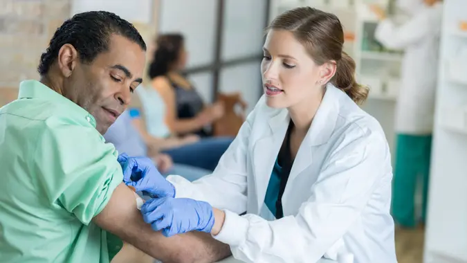 Confident mid adult Caucasian female healthcare professional gently places a bandage on a mature male patient's arm.
