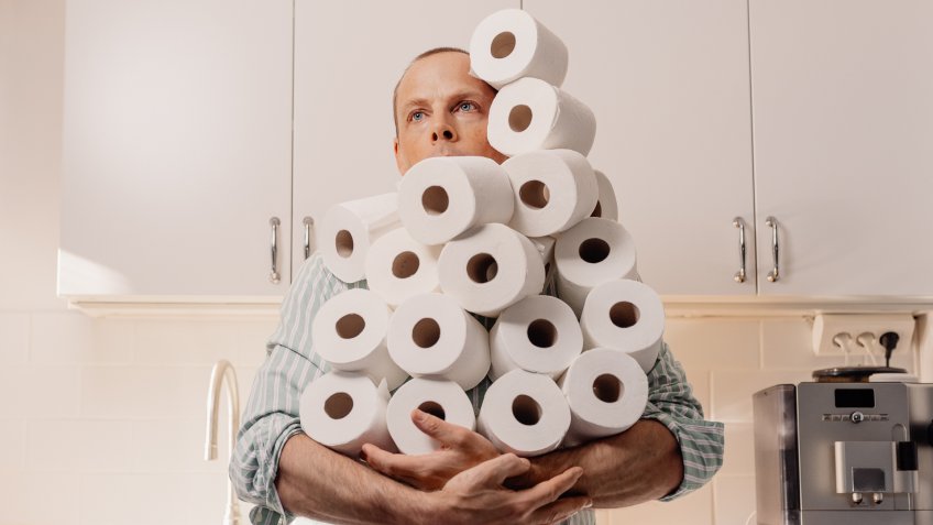Man hoarding toilet paper holding many rollsPhoto taken indoors in kitchen of person holding toilet paper.