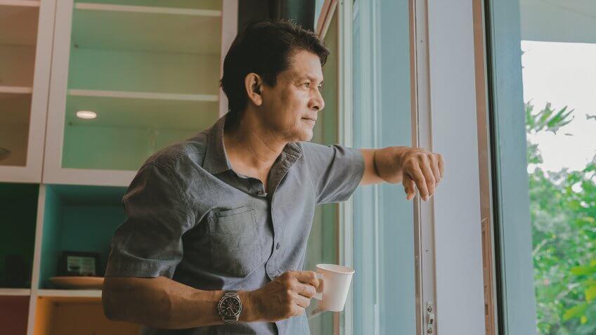 Middle-aged Asian man looking through a window, sipping coffee and using ideas.