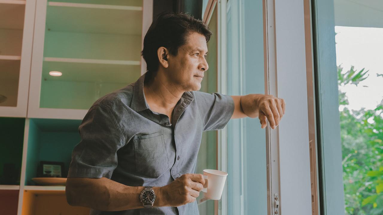 Middle-aged Asian man looking through a window, sipping coffee and using ideas.