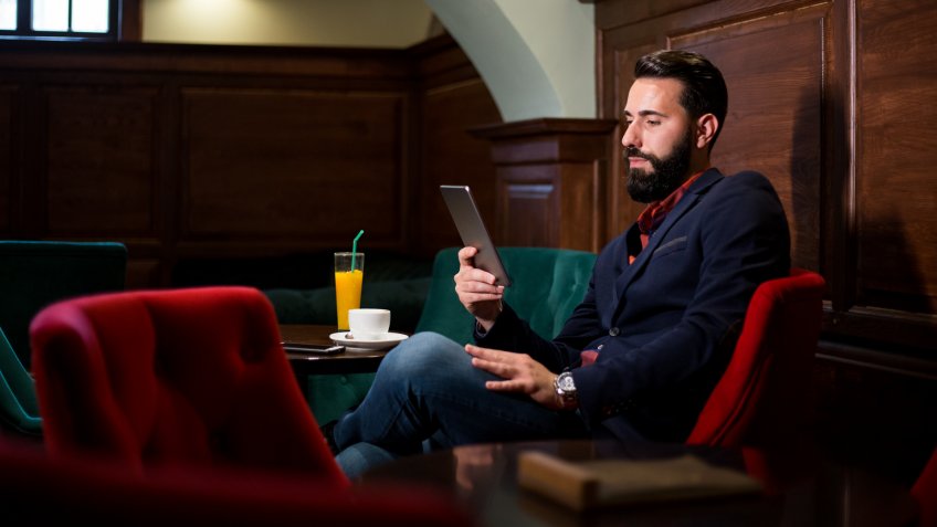 Elegant bearded man drinking coffee and using tablet.