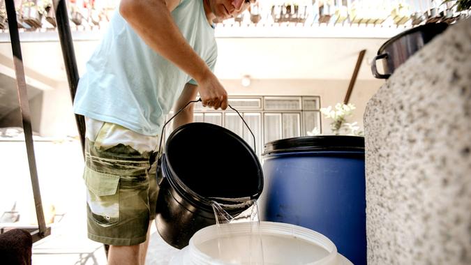 Young man is filling a barrel with water from a bucket.