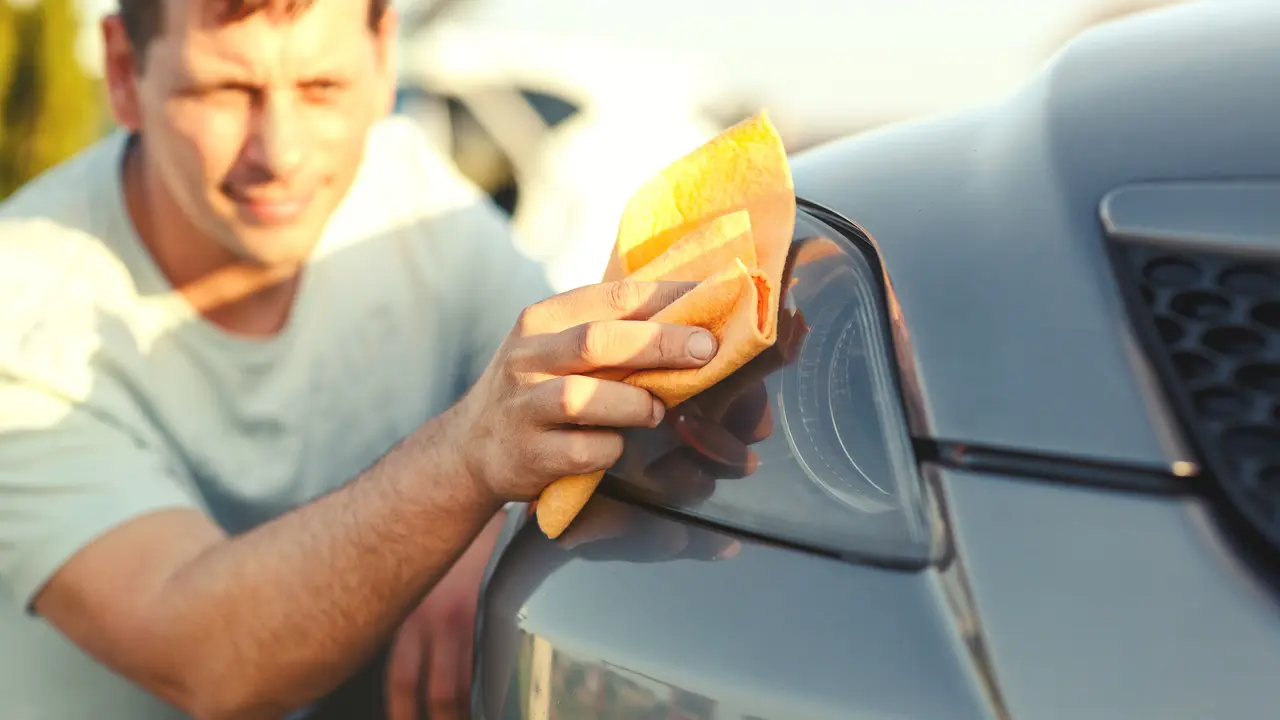 close up of a man cleaning a car with a microfiber cloth, car detailsYoung man washing a car - car washing process with water and washing foam.