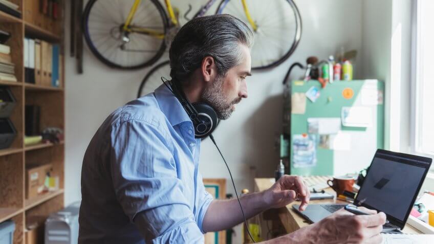 Designer with headphones working at wooden desk in home office.