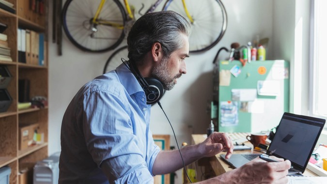 Designer with headphones working at wooden desk in home office.