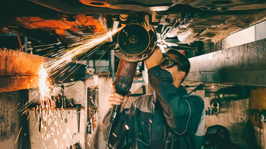 Mechanic using grinding wheel on car bottom making sparks.