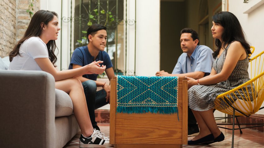 Mexican mother and father sitting with their teenage children and listening to their daughter.