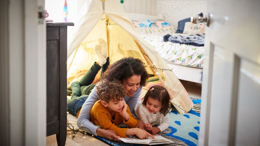 Single Mother Reading With Son And Daughter In Den In Bedroom At Home.