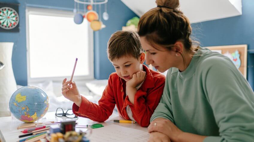 Photo of a young boy being homeschooled by his mother in his bedroom.