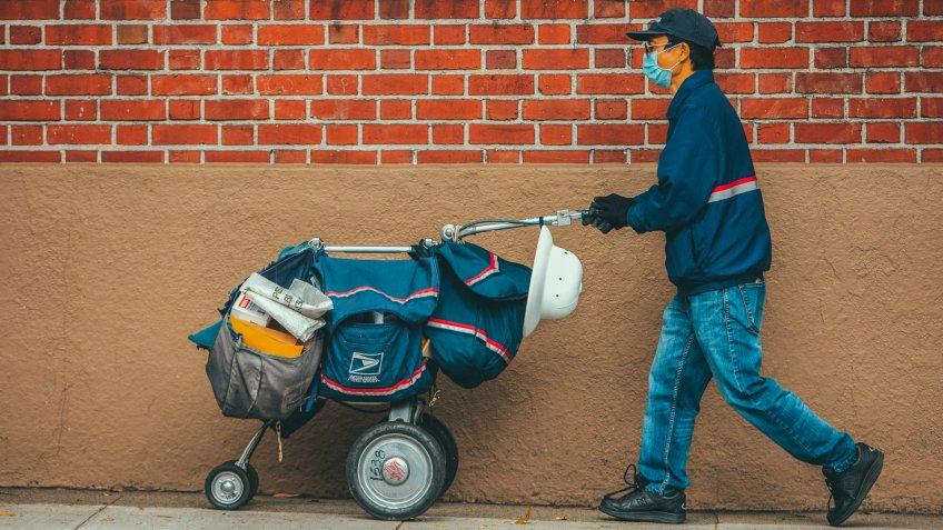 San Francisco, USA - April 4, 2020: San Francisco postal worker in mask delivering mail during stay-at-home order.
