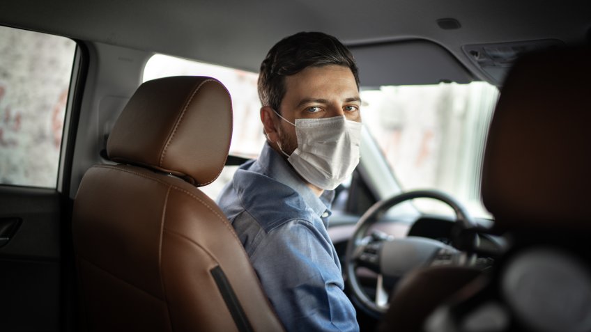 Driver taking to a passenger on seat back wearing protective medical mask.