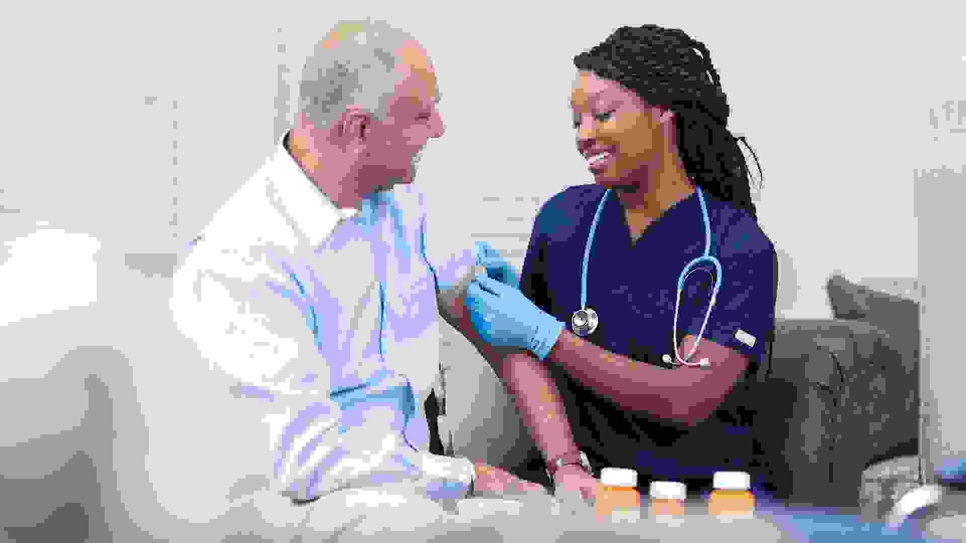 Senior adult, male patient receives vaccine or medicine from his African descent, home healthcare nurse in nursing home or home setting.
