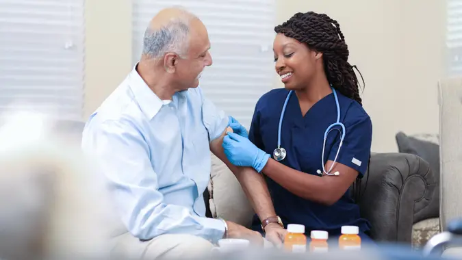 Senior adult, male patient receives vaccine or medicine from his African descent, home healthcare nurse in nursing home or home setting.