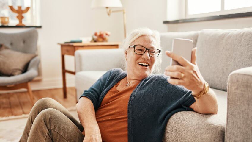 Close up of a senior woman using a phone in the living room.