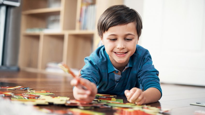 Shot of a little boy lying on the floor while putting together a jigsaw puzzle.
