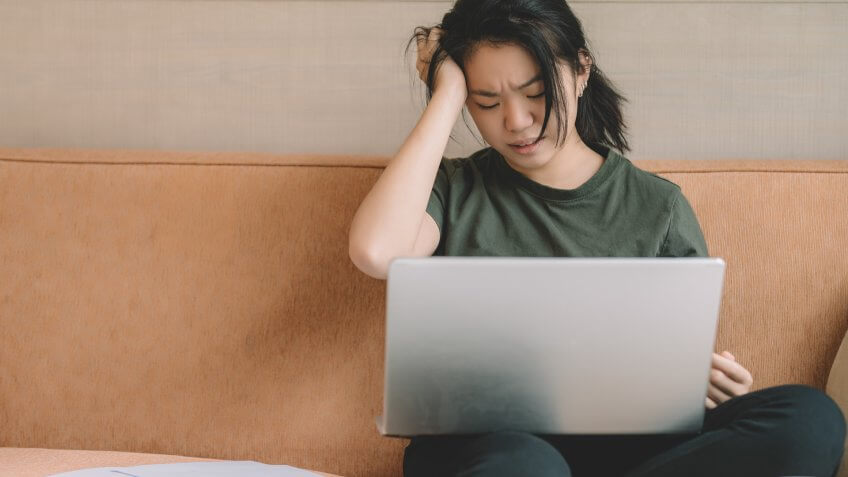 an asian chinese female sitting on sofa with laptop and documents worry and stress on her financial planning.