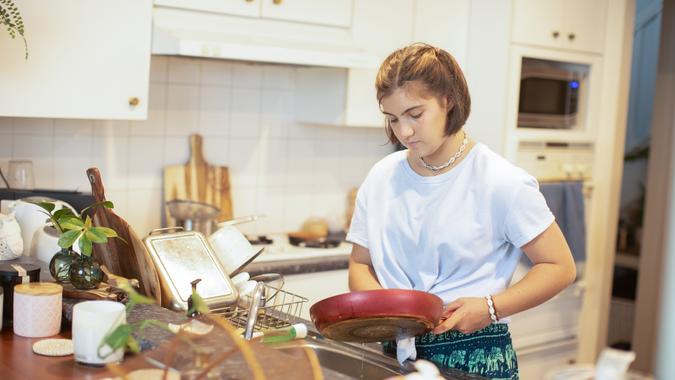 A teenage girls does the washing up at the kitchen sink.