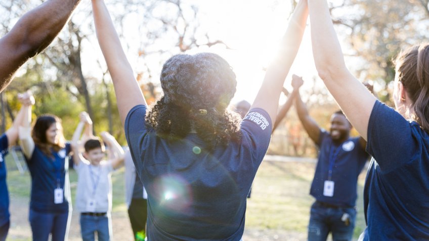 Group of diverse volunteers hold and raise hands in unity after cleaning up their community.