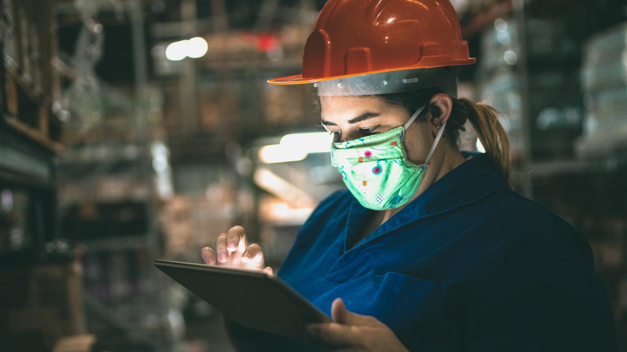 Portrait of mid adult woman wearing face mask using digital tablet - working at warehouse / industry.