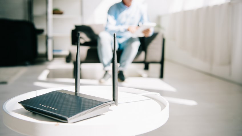 selective focus of black plugged router on white table and businessman sitting on sofa.