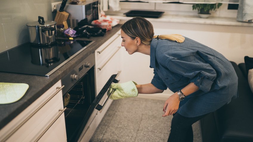 Young woman in kitchen checking food in the oven.