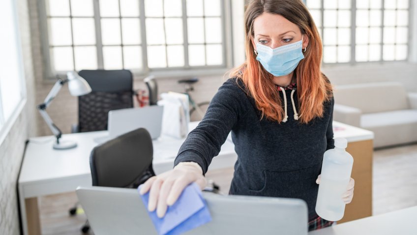 Woman in the office using disinfectant for sanitizing monitor surface during COVID-19 pandemic.