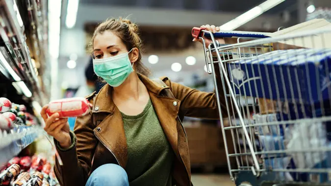 Young woman wearing protective mask and buying food in grocery store during coronavirus pandemic.