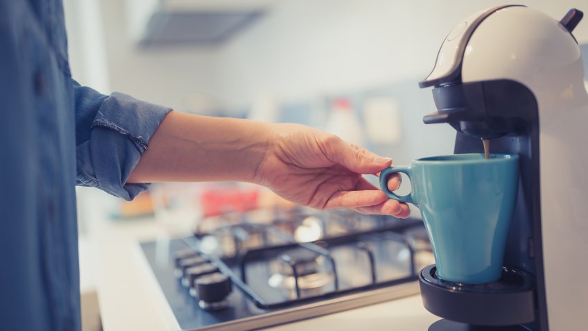Young woman is making her morning coffee in her kitchen.