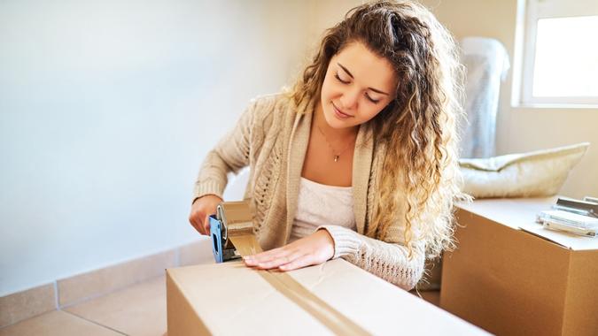 Shot of a young woman sealing a box while moving house.